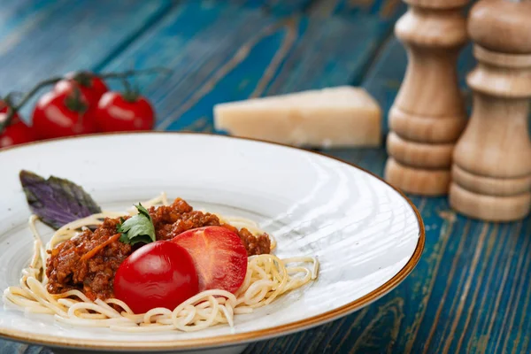 Etli makarna, domates sosu ve mavi ahşap masada sebzeler.