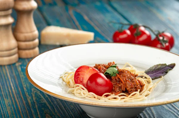 Etli makarna, domates sosu ve mavi ahşap masada sebzeler.