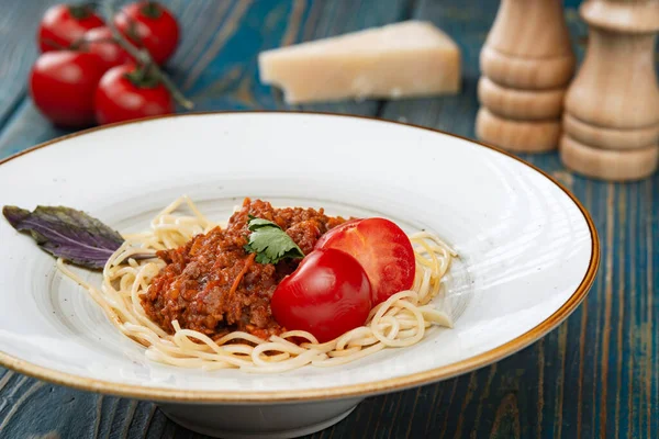 Etli makarna, domates sosu ve mavi ahşap masada sebzeler.