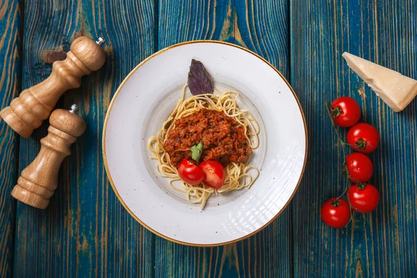 Etli makarna, domates sosu ve mavi ahşap masada sebzeler. en üstteki görünüm