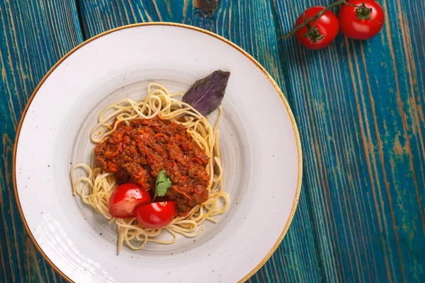 Mavi ahşap arka planda kıyma ve kiraz domatesli lezzetli spagetti. Üst manzara, düz uzanma
