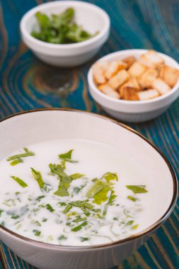 Yoğurt çorbası, mavi ahşap bir masada otlar ve krakerler.