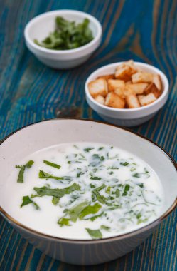 Yoğurt çorbası, mavi ahşap bir masada otlar ve krakerler.