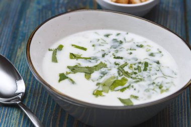Yoğurt çorbası, mavi ahşap bir masada otlar ve krakerler.