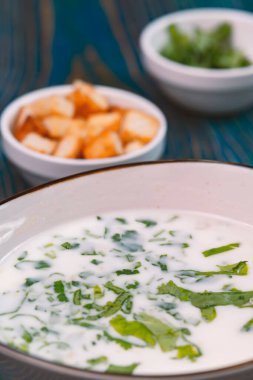 Yoğurt çorbası, mavi ahşap bir masada otlar ve krakerler.