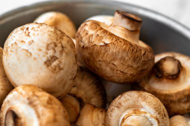 Beyaz ahşap arka planda demir bir kasede çiğ mantar.