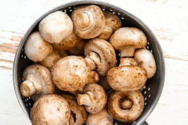 Beyaz ahşap arka planda demir bir kasede çiğ mantar.