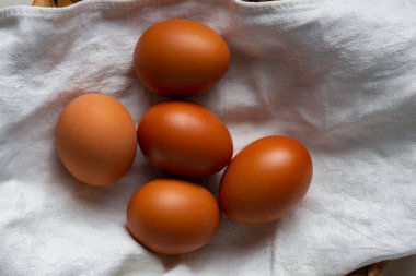 Beyaz havlu ve hasır sepette kahverengi yumurtalar. Üst manzara, düz uzanma