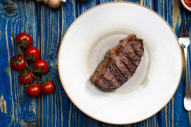Kızarmış biftek, kiraz domatesleri, mavi ahşap masada tuz ve biber..