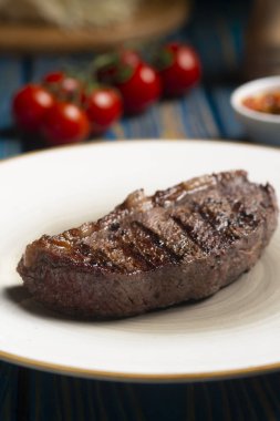 Kızarmış biftek, kiraz domatesleri, mavi ahşap masada tuz ve biber..