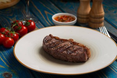 Kızarmış biftek, kiraz domatesleri, mavi ahşap masada tuz ve biber..