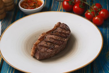 Kızarmış biftek, kiraz domatesleri, mavi ahşap masada tuz ve biber..