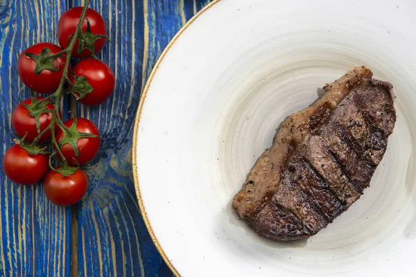 Izgara biftek, kiraz domatesleri ahşap masada tuz ve biber..