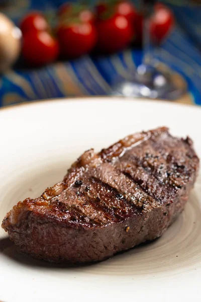 Kızarmış biftek, kiraz domatesleri, mavi ahşap masada tuz ve biber..