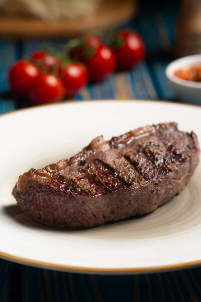 Roasted steak ,cherry tomatoes, salt and pepper on blue wooden table.