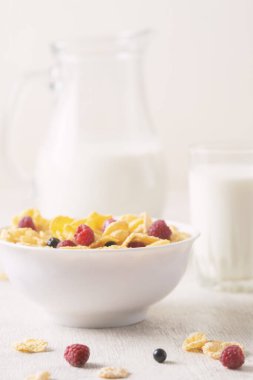 Beyaz arka planda ahududu ve yaban mersinli mısır gevreği. Kahvaltı. Böğürtlenli ve sütlü mısır gevreği. Mısır gevreği. Taze sağlıklı yiyecekler. Sabah yemeği. Tahta masa. Organik. Diyet kavramı.