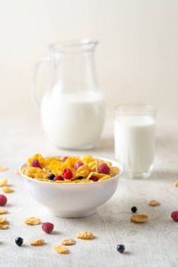 Mısır gevreği, yaban mersini ve ahududu ile sağlıklı kahvaltı. Sağlıklı mısır gevreği, beyaz masa üzerinde süt ve böğürtlen ile kase. Meyveli lezzetli yuvarlak mısır gevreği. Diyet kavramı.