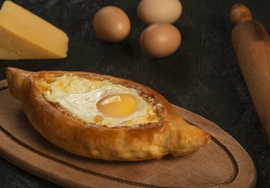 Adjarian, Gürcü khachapuri yumurtası ve peynirli geleneksel mutfağı siyah arka planda.