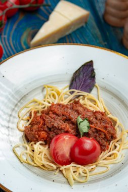 Beyaz tabakta spagetti bolonez makarna, tuz, biber, peynir ve domates mavi ahşap arka planda..