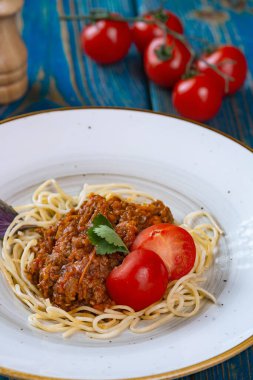 Etli makarna, domates sosu ve mavi ahşap masada sebzeler.