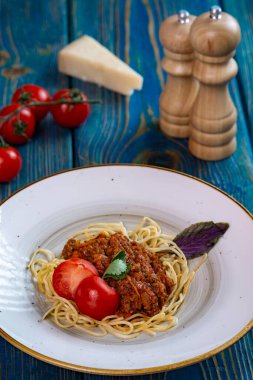 Beyaz tabakta spagetti bolonez makarna, tuz, biber, peynir ve domates mavi ahşap arka planda..