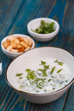 Yoğurt çorbası, mavi ahşap bir masada otlar ve krakerler.