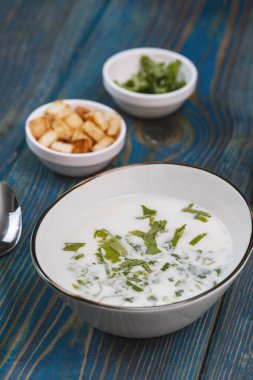 Yoğurt çorbası, mavi ahşap bir masada otlar ve krakerler.