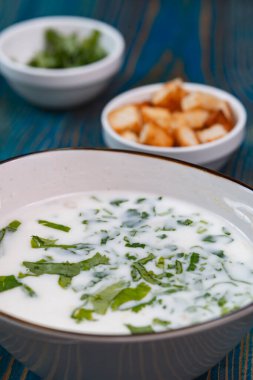 Yoğurt çorbası, mavi ahşap bir masada otlar ve krakerler.