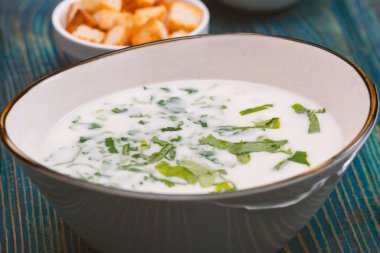 Yoğurt çorbası, mavi ahşap bir masada otlar ve krakerler.