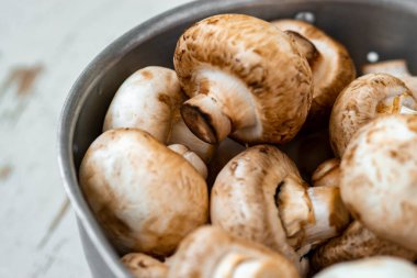 Beyaz ahşap arka planda demir bir kasede çiğ mantar.