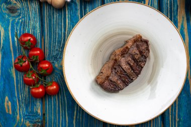 Kızarmış biftek, kiraz domatesleri, mavi ahşap masada tuz ve biber..