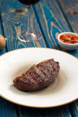 Taze ızgara et. Mavi ahşap arka planda beyaz tabakta baharatlı biftekler.