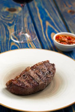 Mavi ahşap arka planda beyaz tabakta baharatlı ızgara biftek.