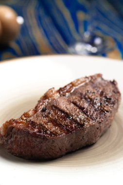 Mavi ahşap arka planda beyaz tabakta baharatlı ızgara biftek.