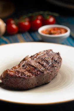Kızarmış biftek, kiraz domatesleri, mavi ahşap masada tuz ve biber..