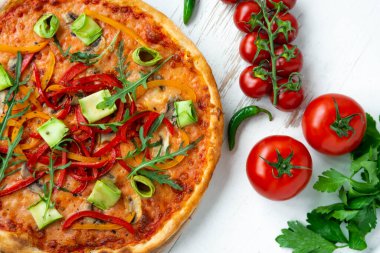 Peynirli, domatesli, biberli ve ahşap masadaki avokadolu vejetaryen pizzası.