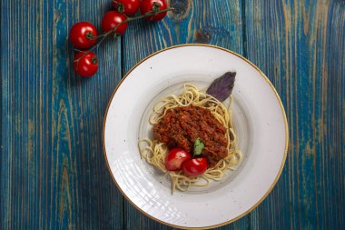 Etli makarna, domates sosu ve mavi ahşap masada sebzeler. en üstteki görünüm