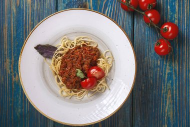 Beyaz tabakta spagetti bolonez makarna, tuz, biber, peynir ve domatesler mavi ahşap arka planda.