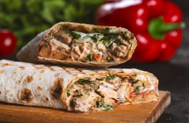 Shawarma sandviçi taze rulo, ızgara et ve siyah arka planda beyaz soslu salata..