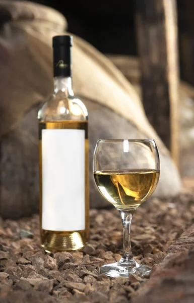 Glass and bottle of white wine in the wine cellar. Bottle with a label-preparation for designers