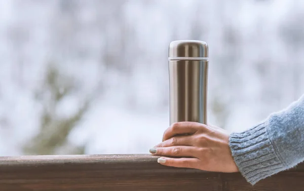 Woman in the background of a winter forest in a thermos bottle in hands