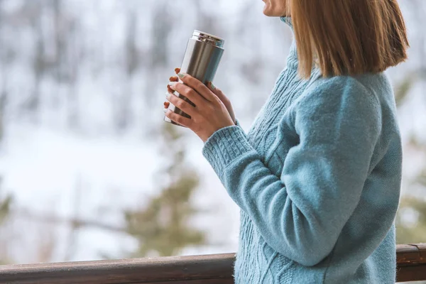 Woman in the background of a winter forest in a thermos bottle in hands