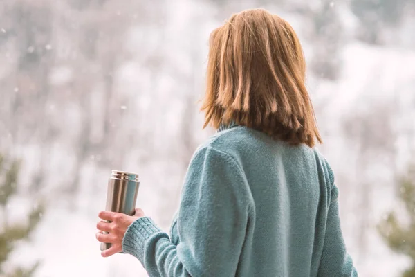 Woman in the background of a winter forest in a thermos bottle in hands