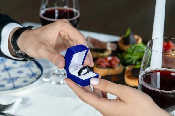 Male hands with blue velvet box containing payments smart ring. Man gives a woman payments smart ring.  Romantic dinner. Valentine day