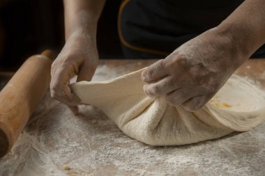 Ahşap bir masada hamur yoğuran bir kadının elleri
