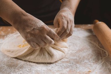 Ahşap bir masada hamur yoğuran bir kadının elleri