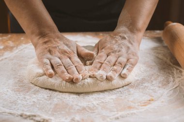 Ahşap bir masada hamur yoğuran bir kadının elleri