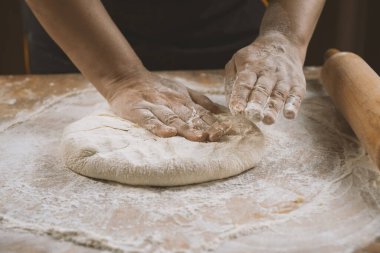 Hands of a woman kneading dough on a wooden table