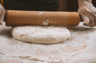 Şef masada merdaneyle hamuru yuvarlıyor. Eller yakın plan. Makarna, ekmek, spagetti, khachapuri, yemek konsepti.
