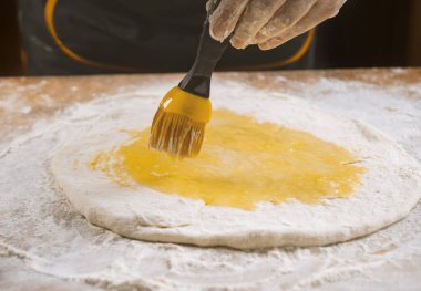 Pizza hamuru, aşçı mutfakta yumurta sarısı ve pasta fırçası sürüyor.
